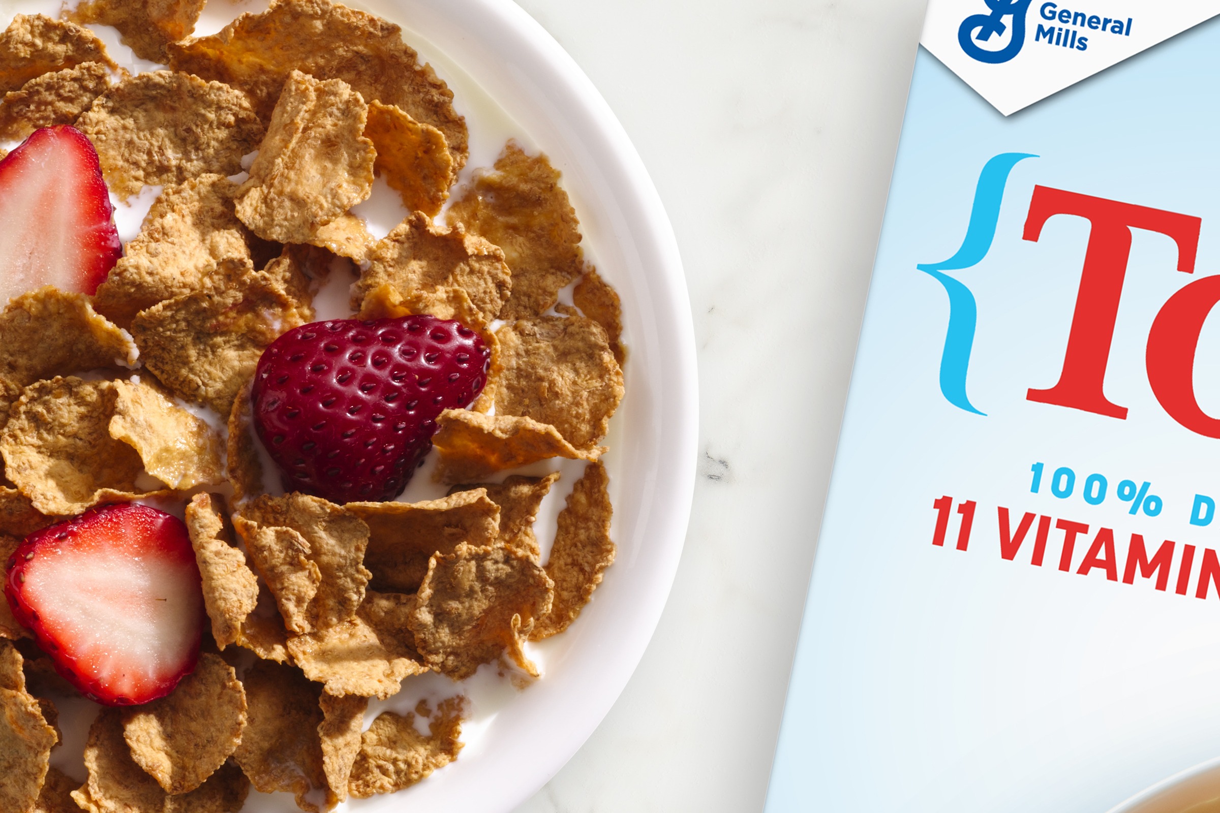 Bowl of Total cereal with strawberries on top of the cereal, and next to the box